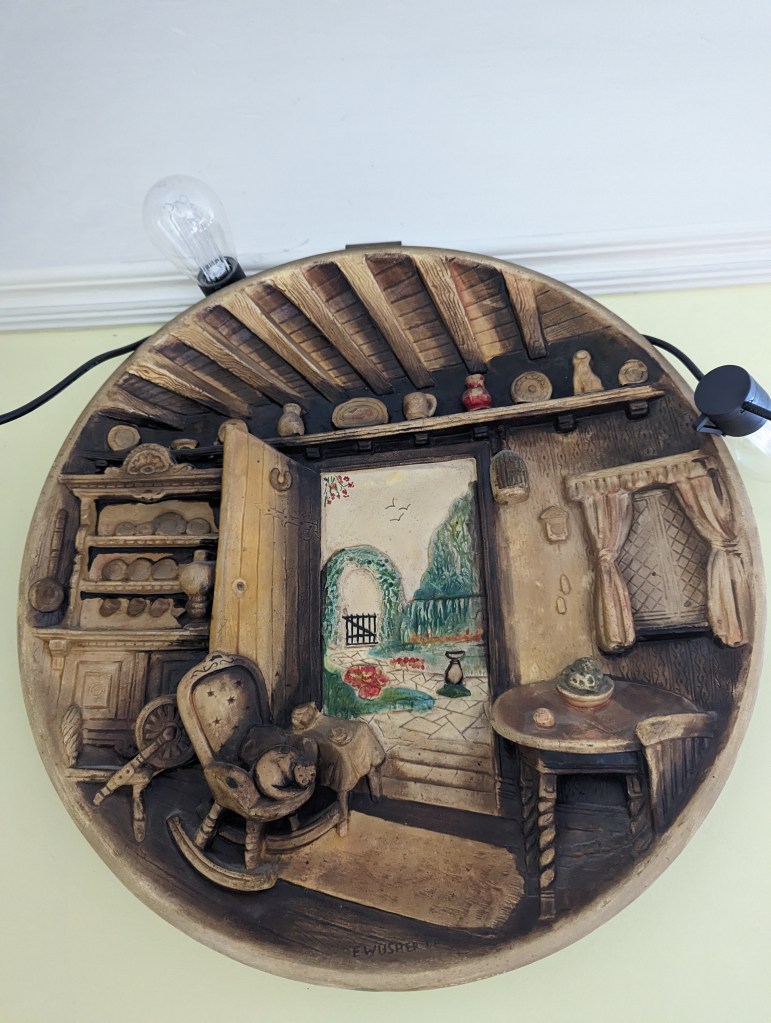 Country Cottage chalkware plate featuring a brown cottage interior with the door open showing a sunny and idyllic garden