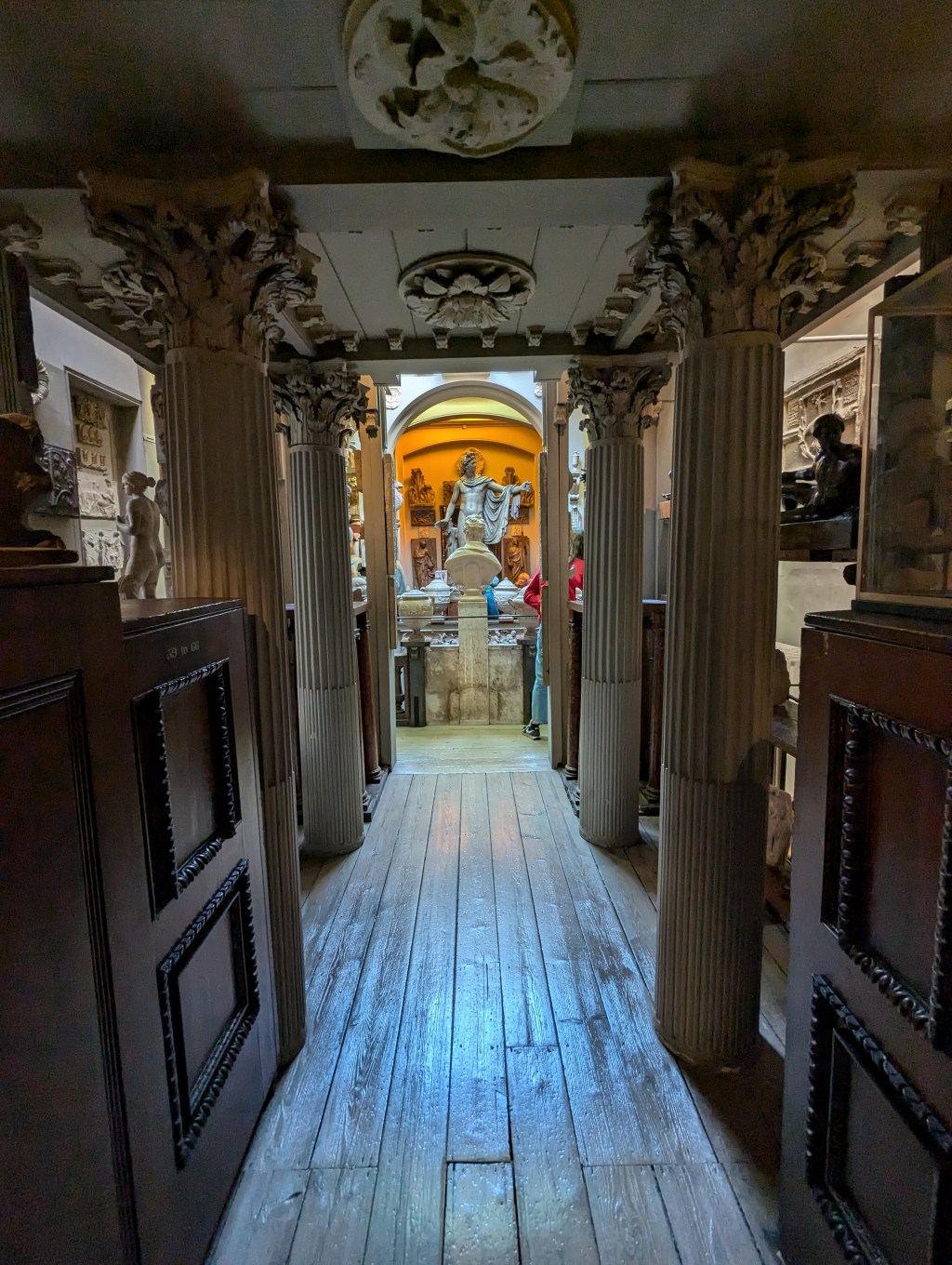 A narrow corridor, bordered by columns, framing a statue against an orange background
