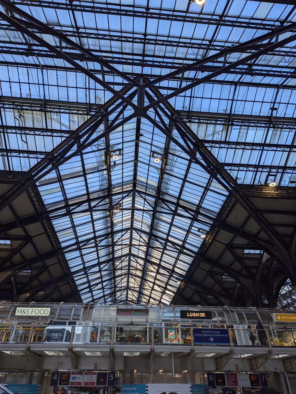 A cast iron and glass station roof through which the blue sky can be seen.