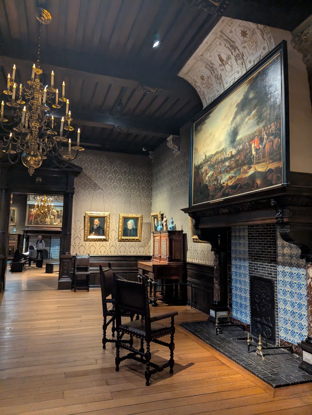 The interior of a sixteenth century room in a wealthy printer's house. The room has a large fireplace, a chandelier, and paintings on the walls.
