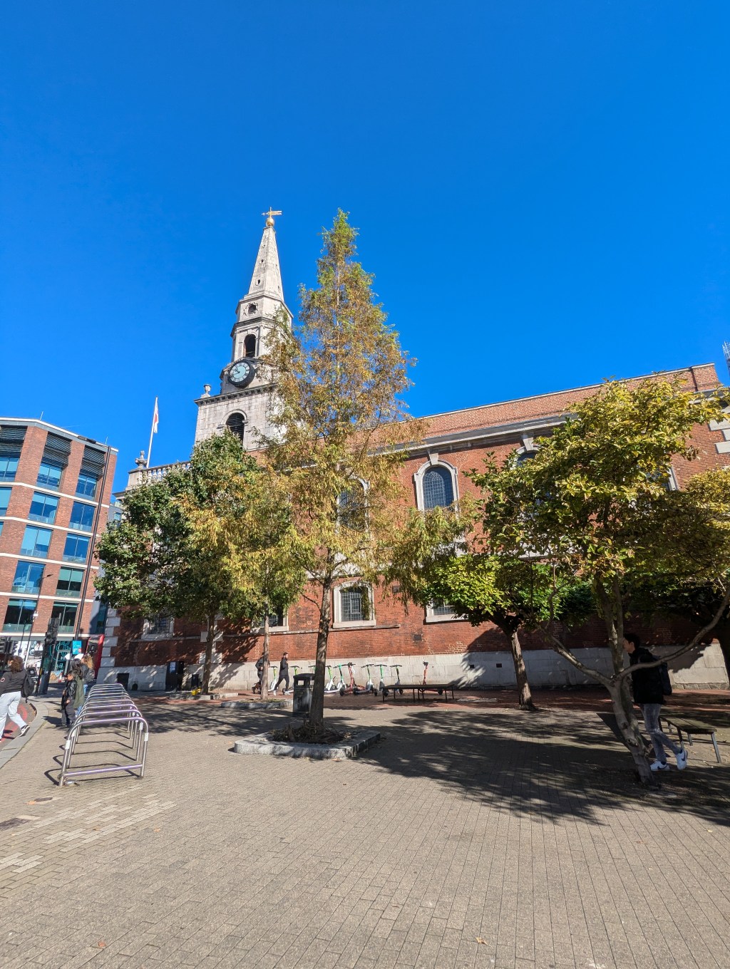 A church with spire is surrounded by trees in brilliant sunshine with a bright blue sky