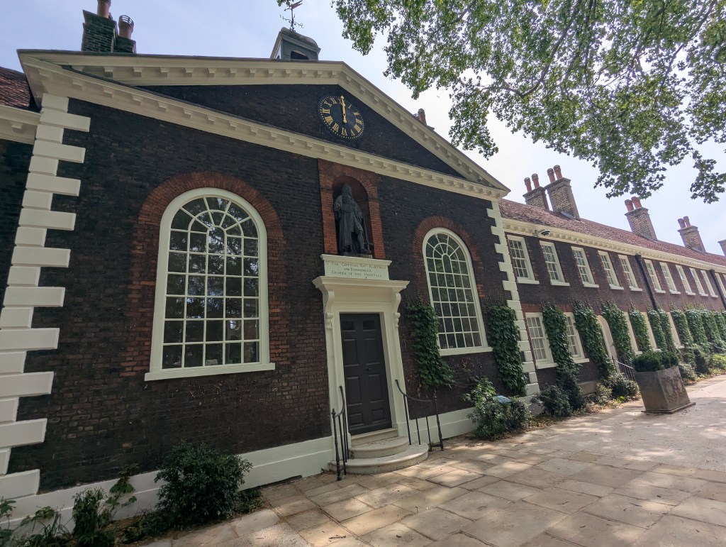 The Museum of the Home, Hackney. A dark brick building with white stone window frames and accents. A tree can be see framing the building , creating a park-like garden